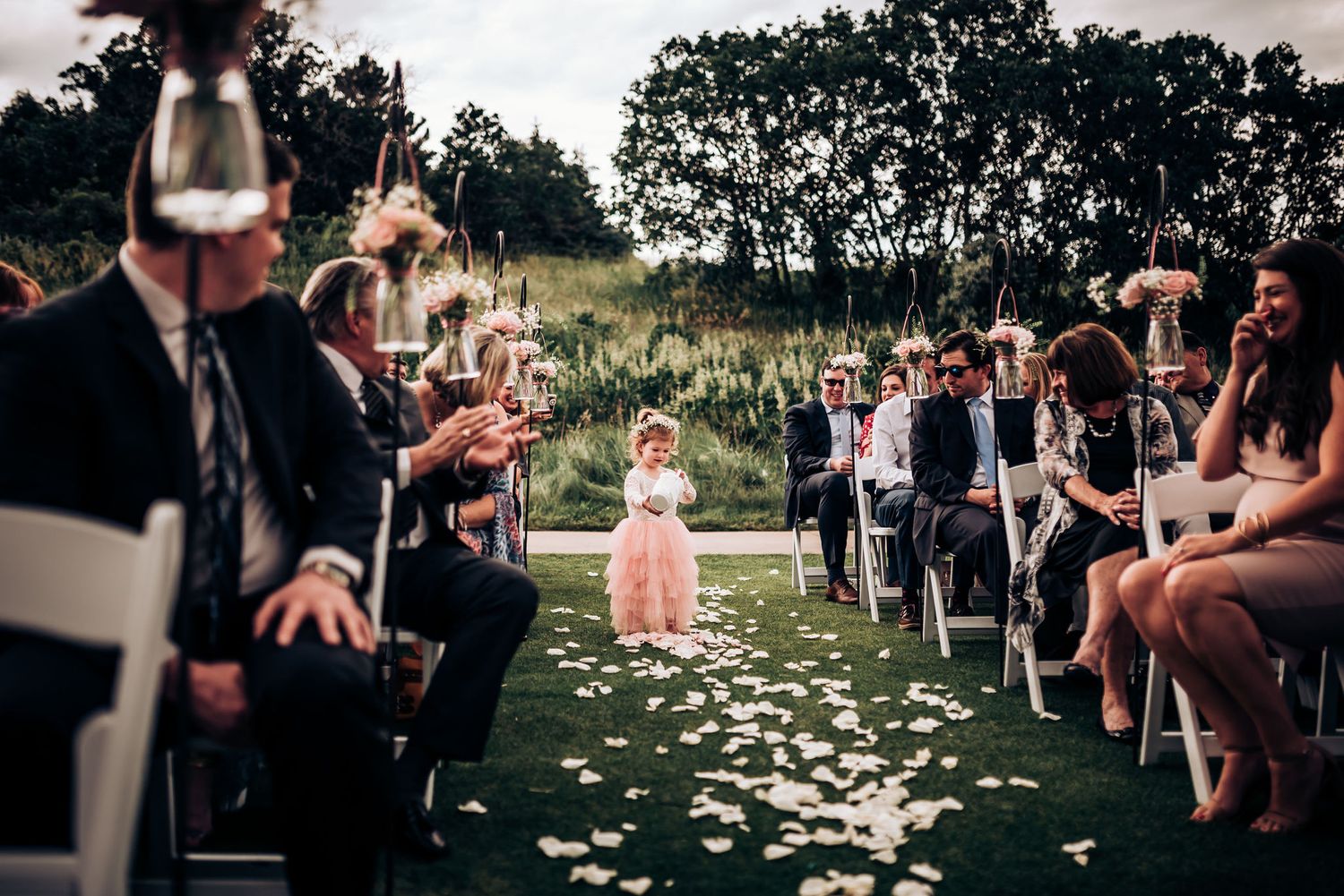 Guests line both sides of petal-strewn aisle during outdoor wedding ceremony.