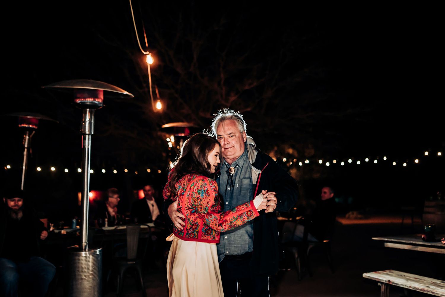 Couple dancing together at nighttime outdoor celebration with string lights and heaters.