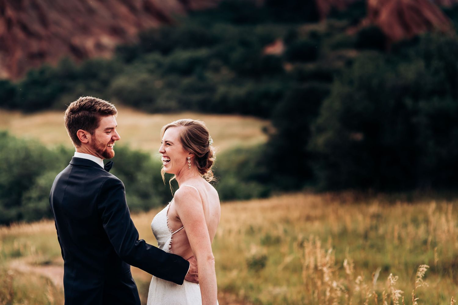 Romantic wedding moment captured in a golden field with mountain landscape backdrop.