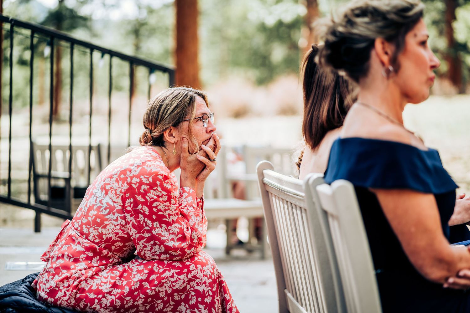 Guest in floral dress shows emotional reaction during outdoor wedding ceremony.