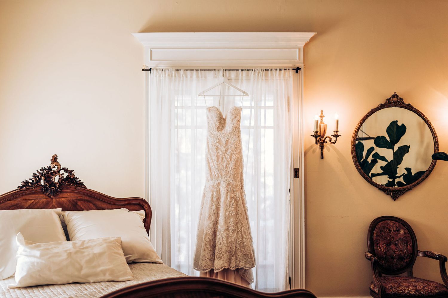 Vintage-inspired wedding gown displayed in sunlit bedroom with antique furniture and decor.