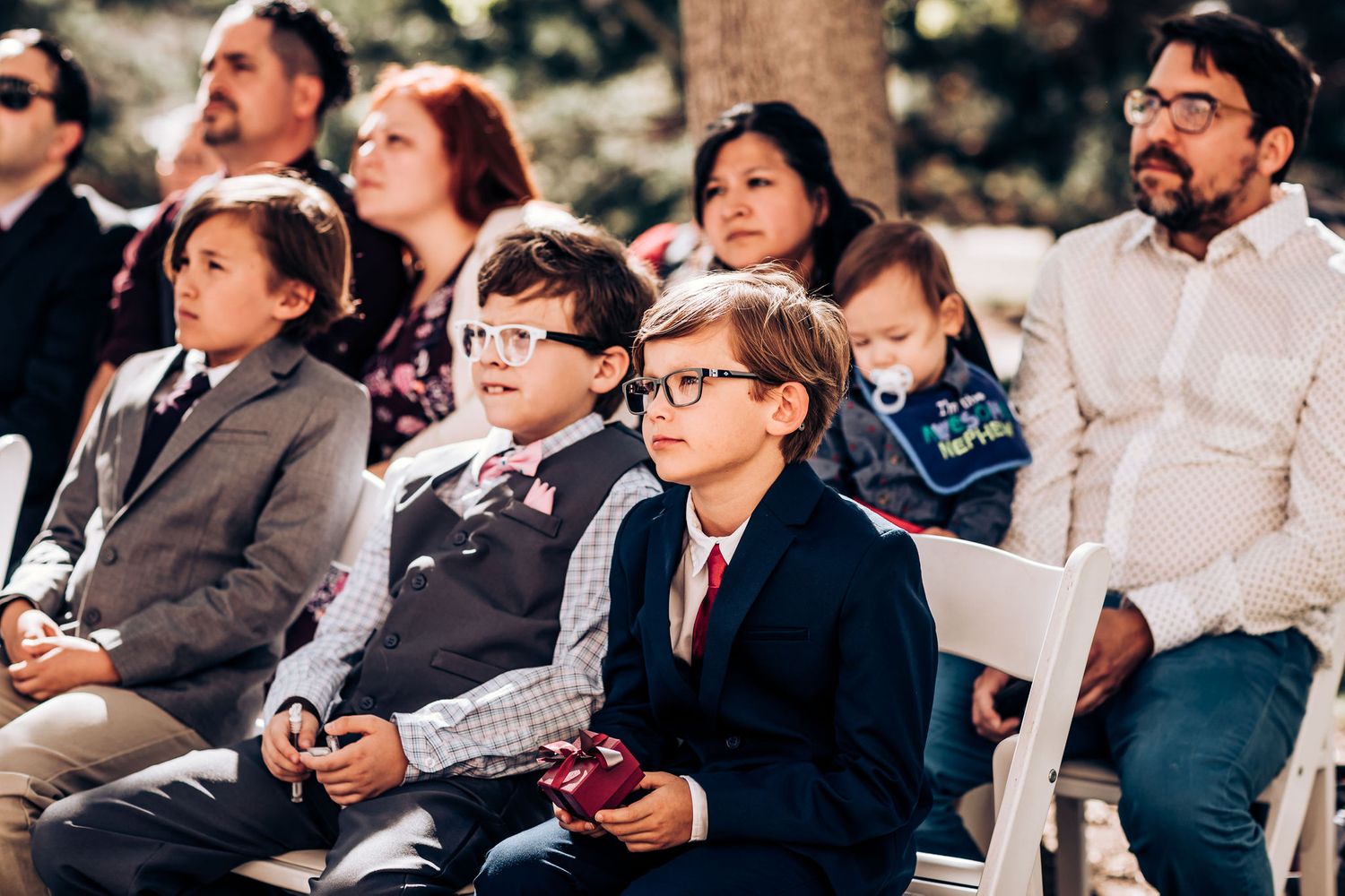 Wedding guests seated in white chairs watching the outdoor ceremony.