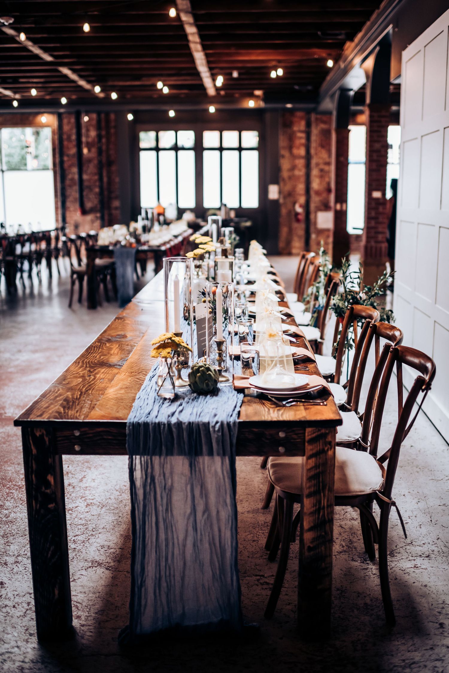 Long wooden dining table with navy runner and place settings in industrial brick venue.