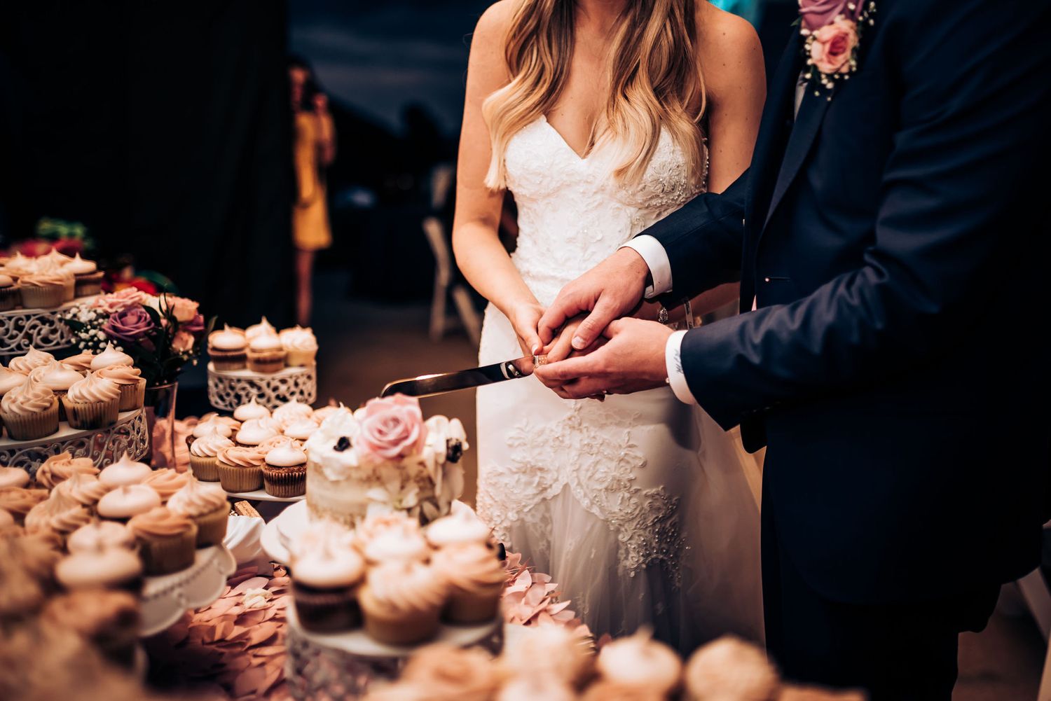 Couple cutting desserts at wedding reception dessert display table.