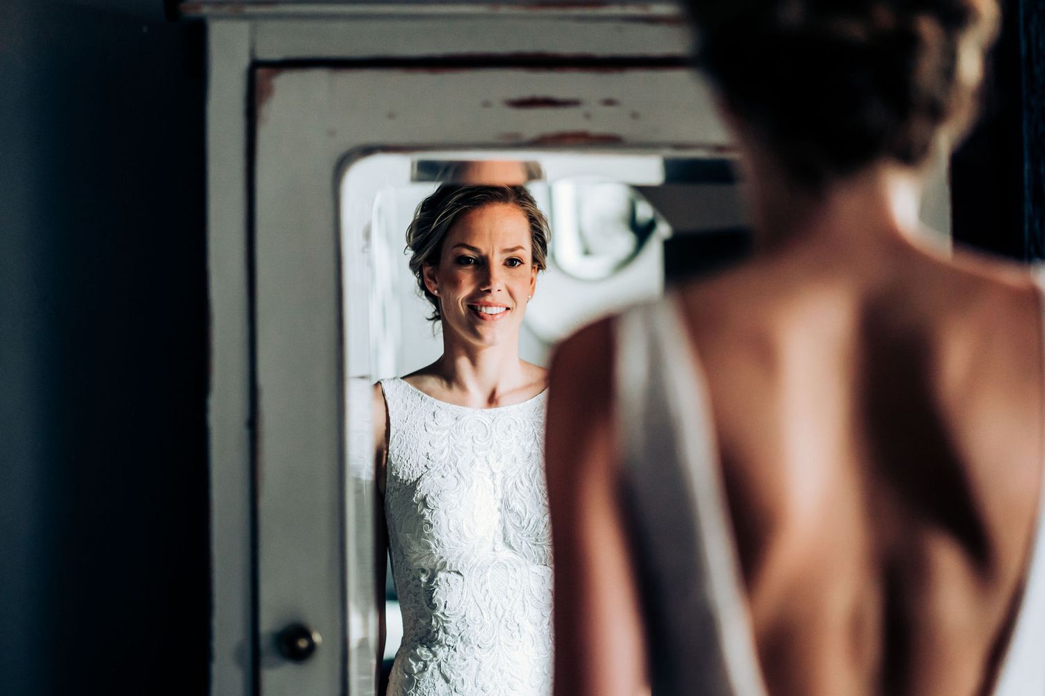 A white lace wedding dress reflects in a vintage mirror during bridal preparations.