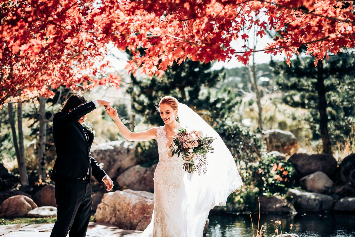 A romantic wedding moment under vibrant red autumn foliage beside a garden pond.