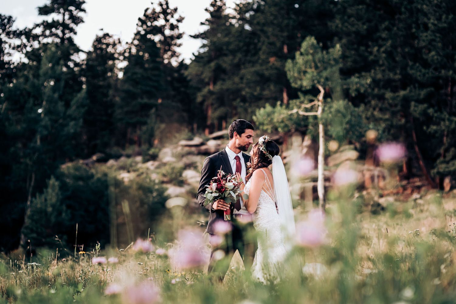 Outdoor wedding photography in mountain meadow with wildflowers and pine trees.