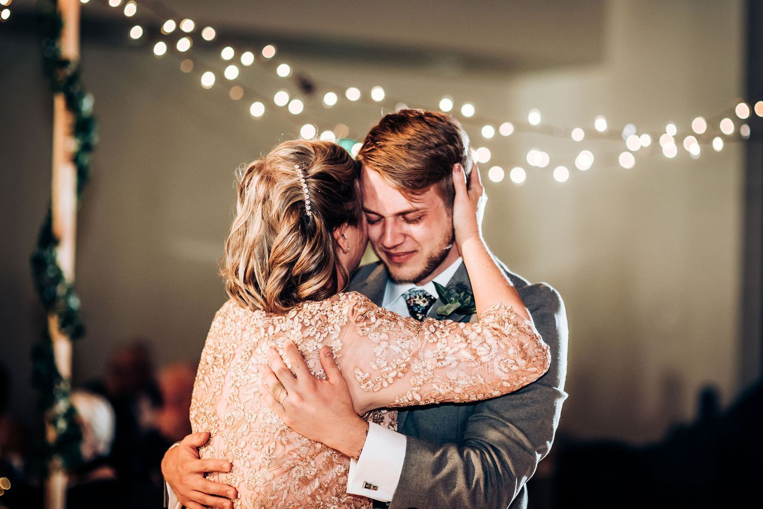 Tender embrace during a romantic dance beneath glowing string lights at evening celebration.