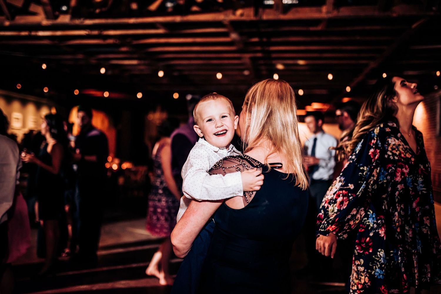 Joyful moment between guests at a wedding reception with a smiling baby in view.