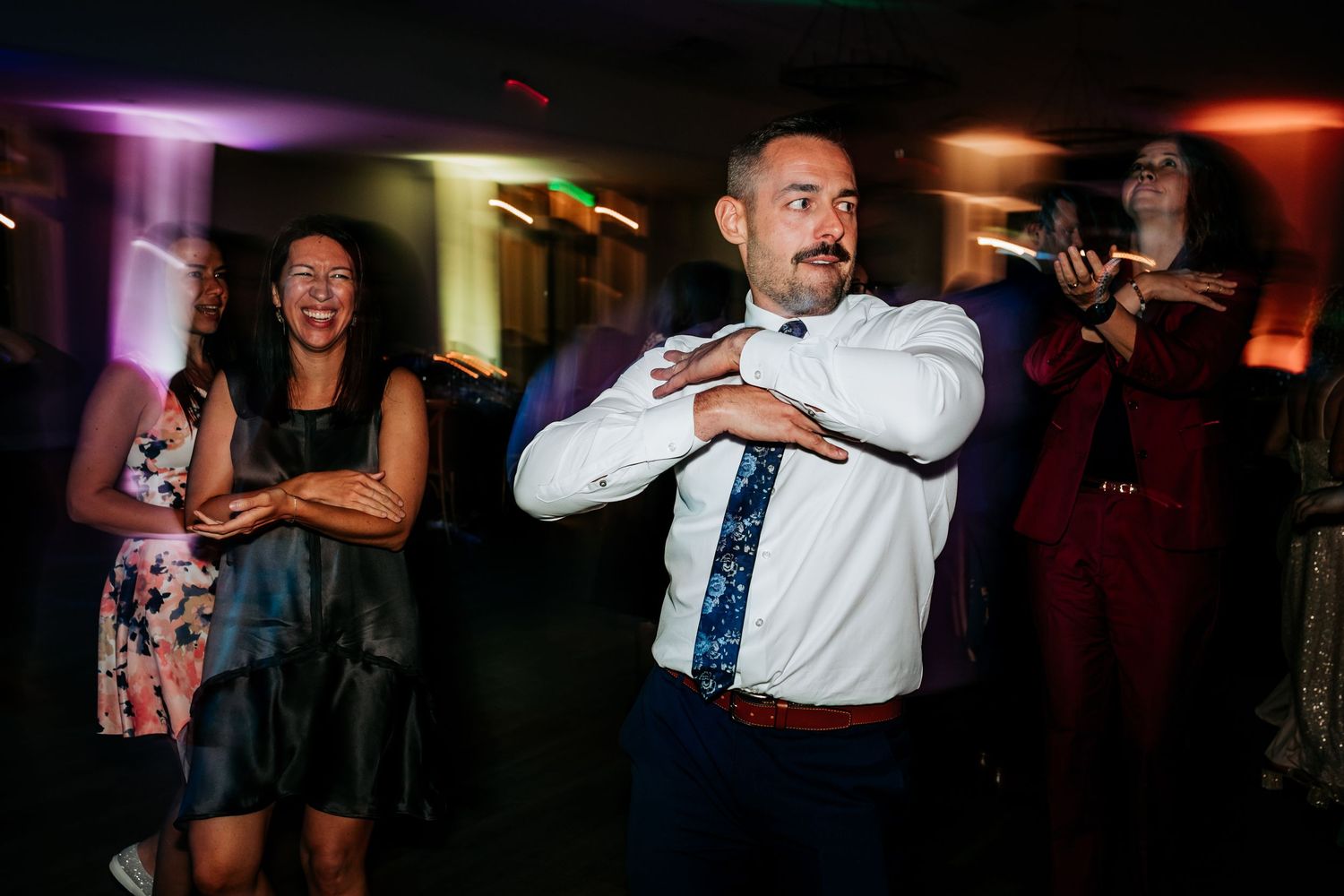 Man in white dress shirt and tie dancing at a lively wedding reception celebration.