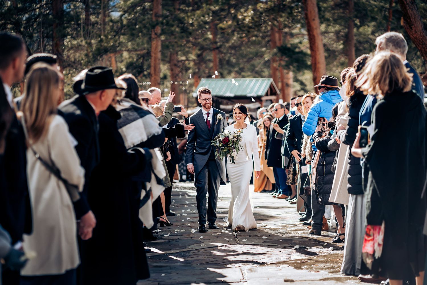 Wedding procession through forest path with guests lining both sides.