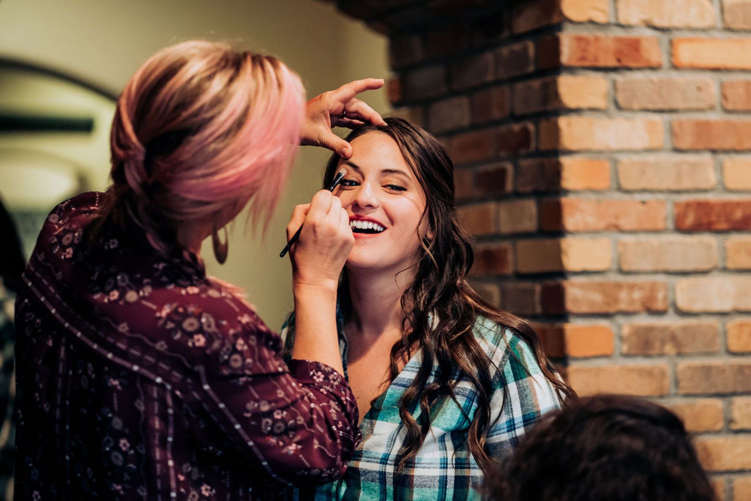 Makeup artist applying cosmetics in front of rustic brick background.