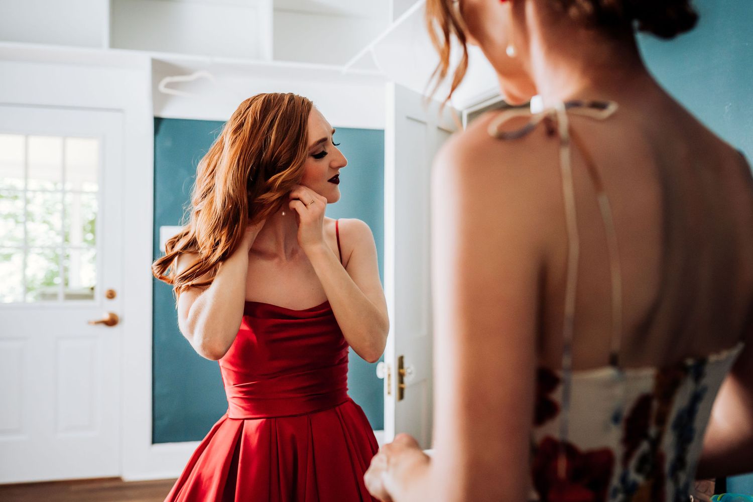 Woman in elegant red dress preparing for special event in bright modern room.