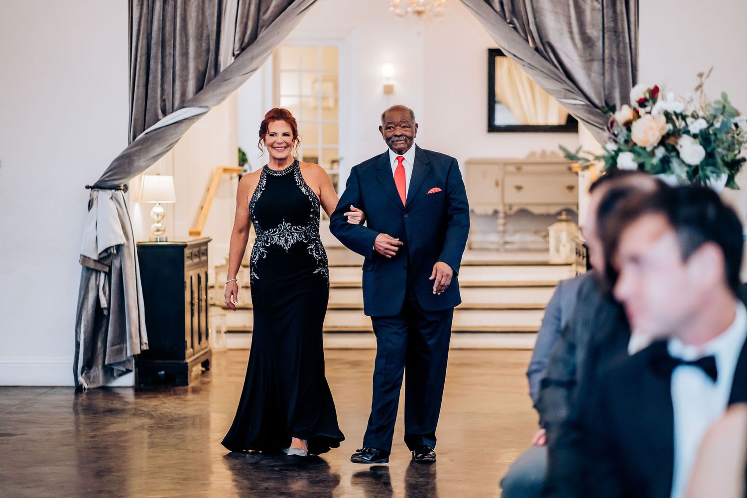 Guests make their entrance at an elegant wedding venue with draped curtains and stairs.