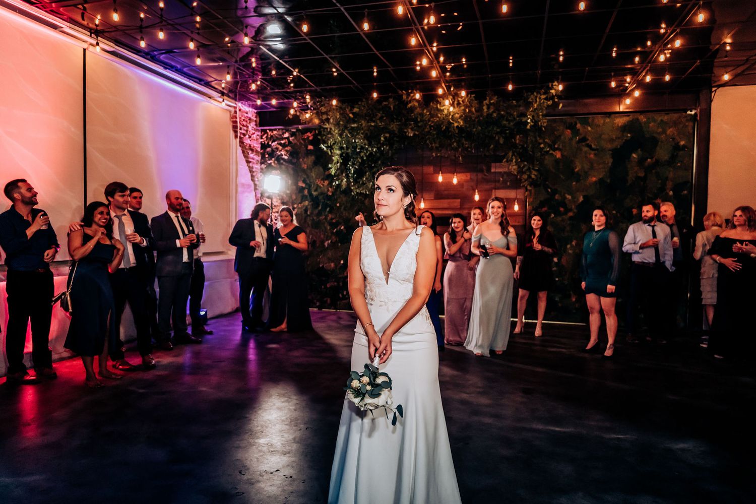 Traditional bouquet toss moment at indoor wedding reception with ambient lighting.