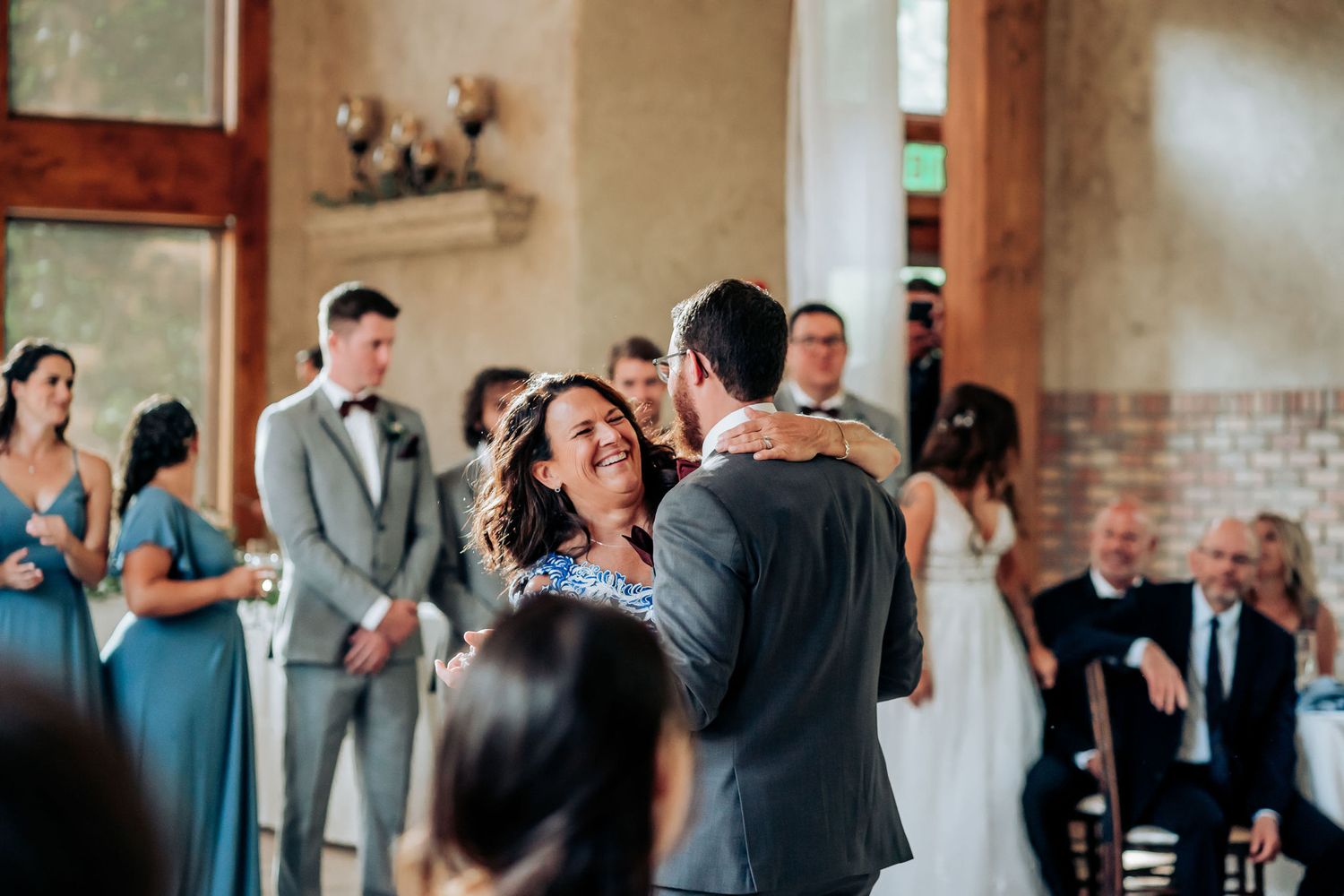 A couple embraces during their first dance at a rustic indoor wedding venue with exposed brick walls.