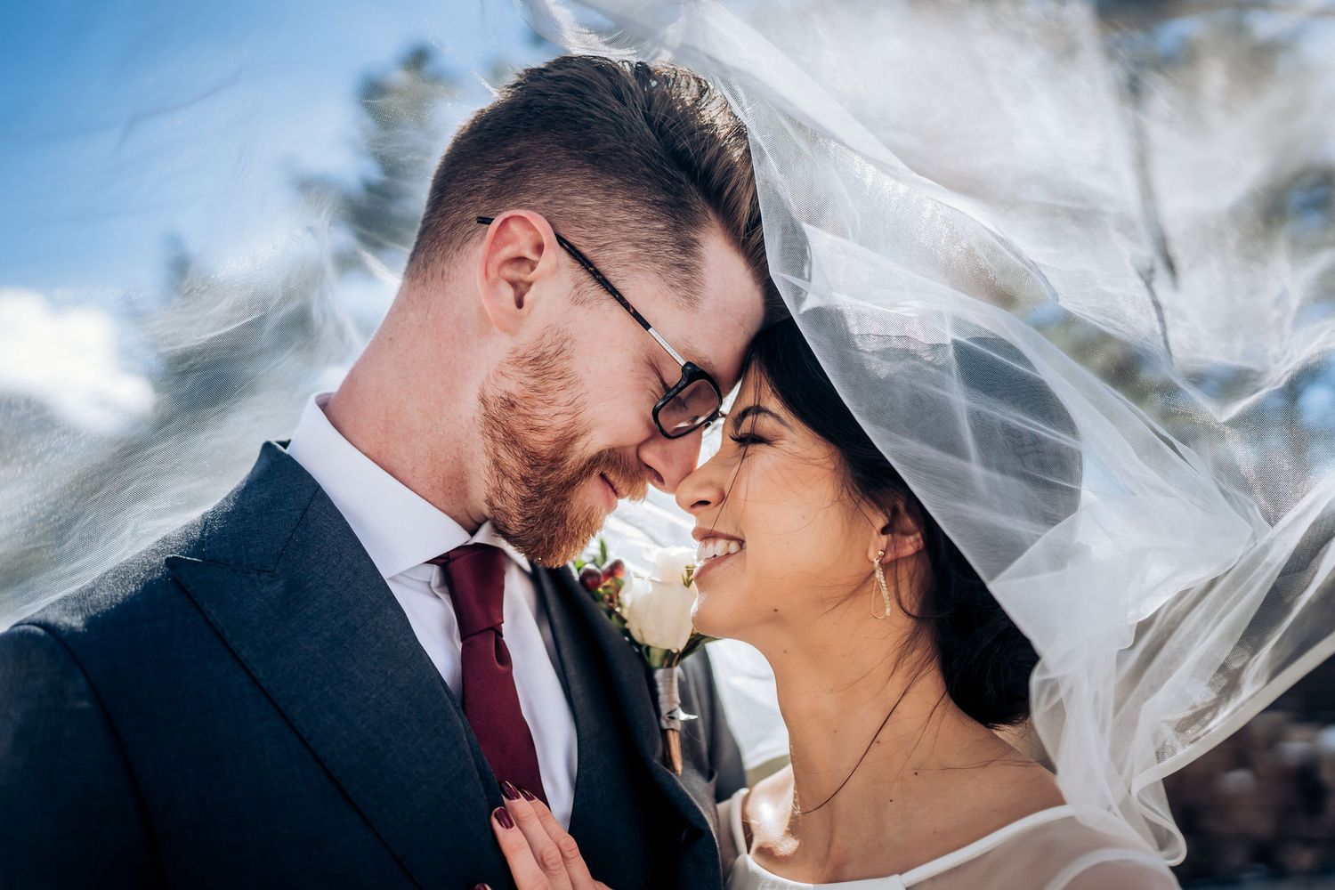 A tender wedding moment captured with flowing veil and winter mountain scenery.
