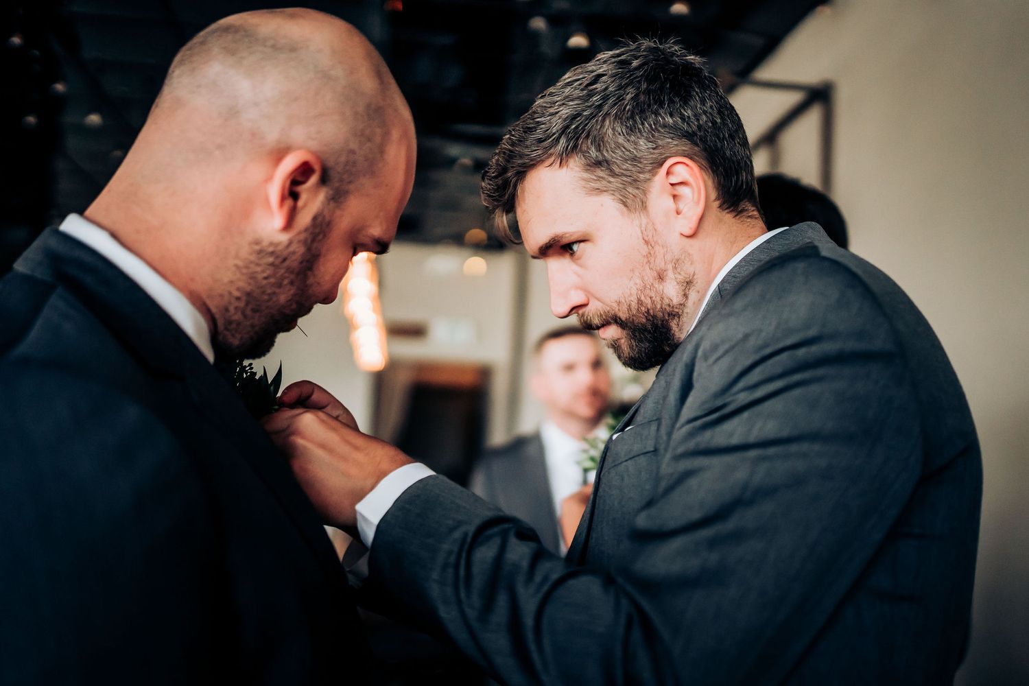 Two people in dark suits adjusting formal attire before an event.
