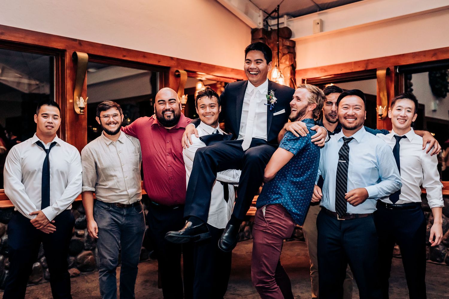 Groomsmen lifting and supporting a member of the wedding party in a playful group photo.
