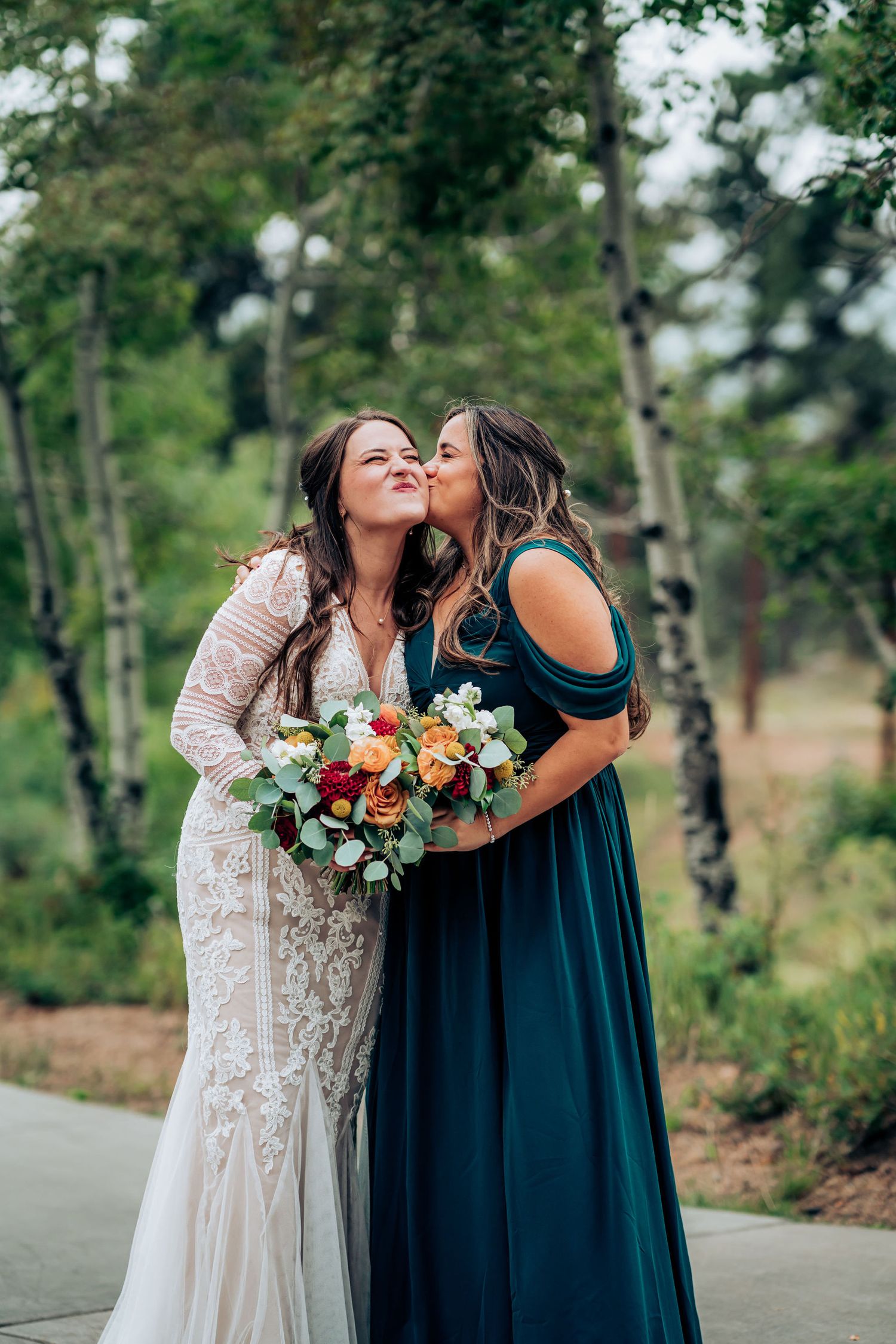 Two wedding party members share an affectionate moment while holding floral bouquets.