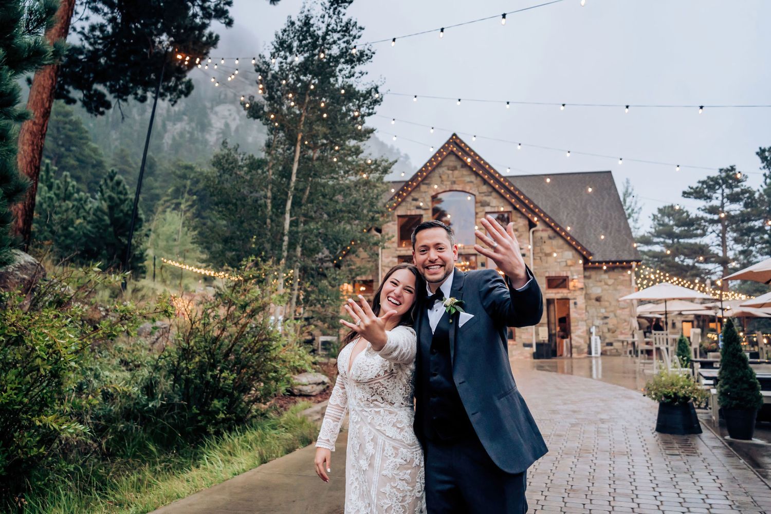 Joyful couple celebrating in front of rustic mountain lodge with string lights.