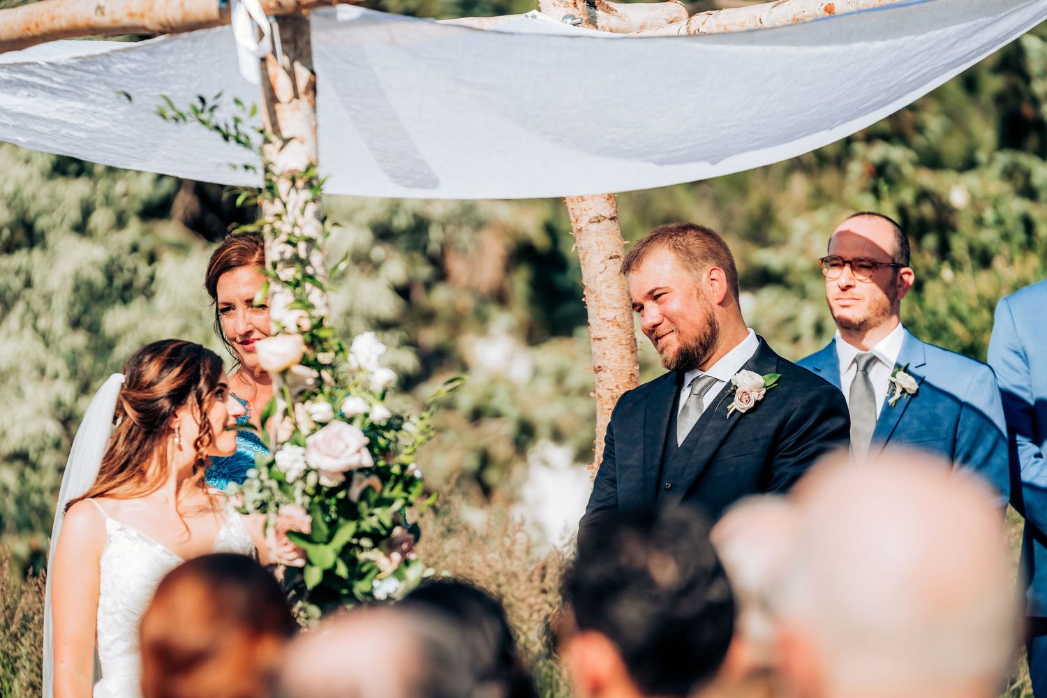 Wedding ceremony under rustic wooden arch with floral decorations and mountain backdrop.