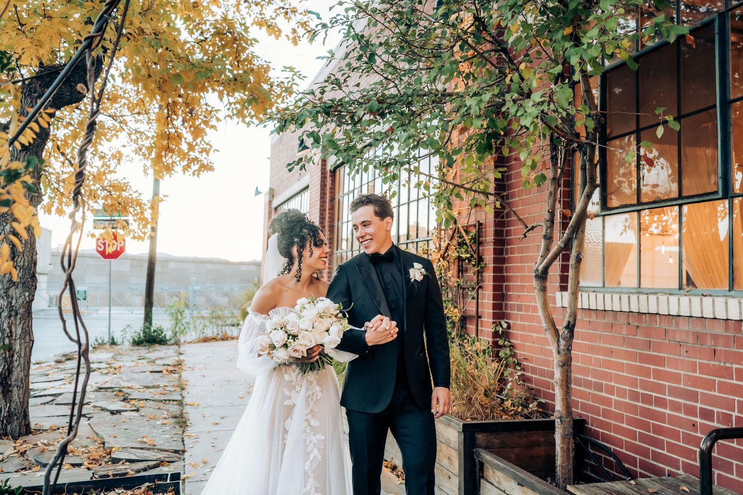 A wedding couple stands together on a brick patio surrounded by autumn foliage.