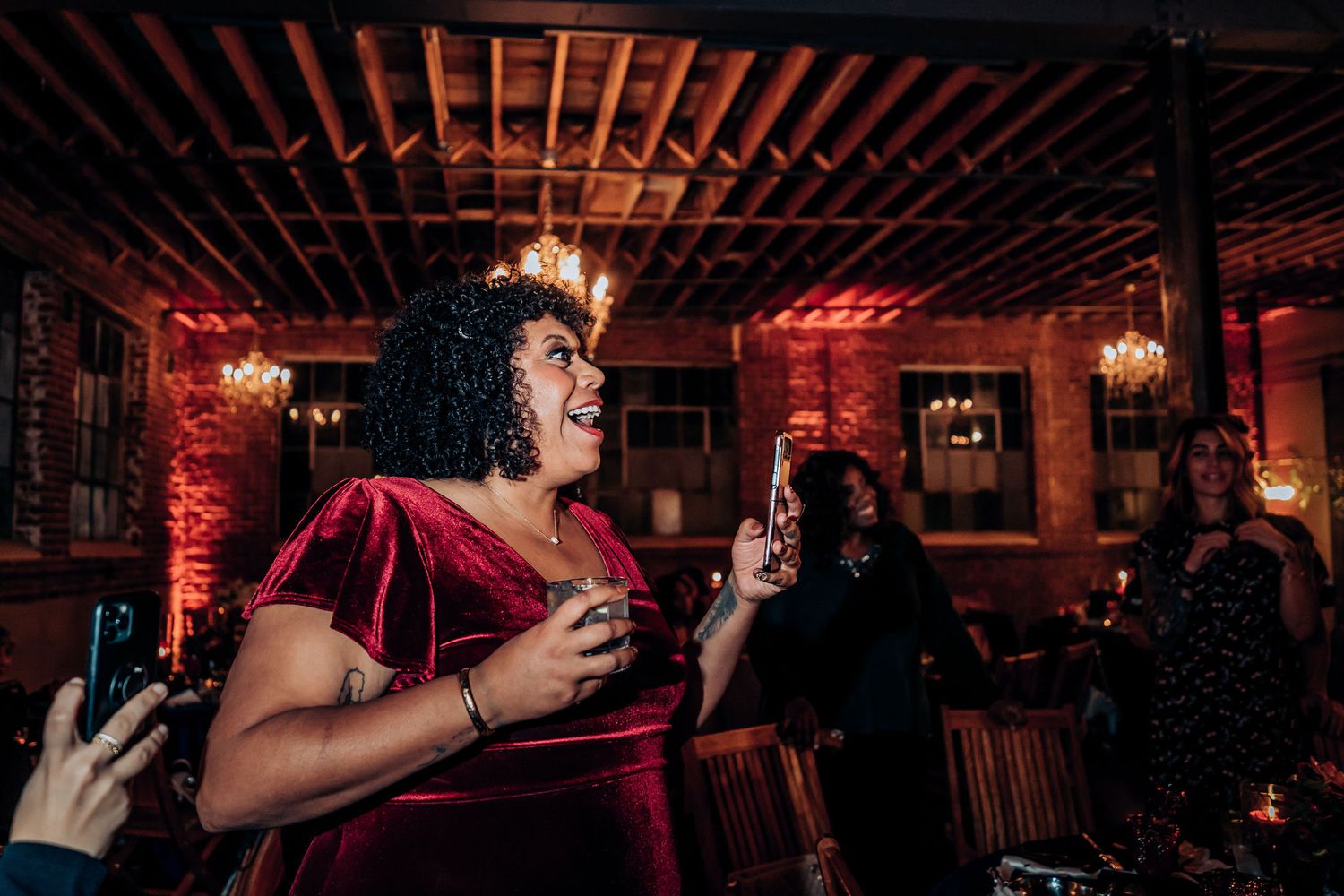 Performer in burgundy velvet dress sings with emotion at an indoor reception.