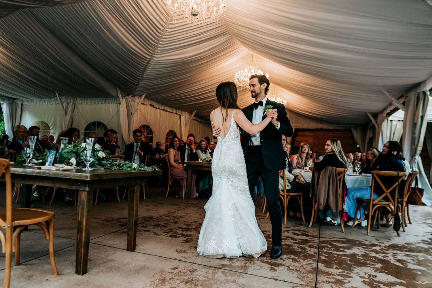 First dance under elegant draped tent at wedding reception with rustic decor.