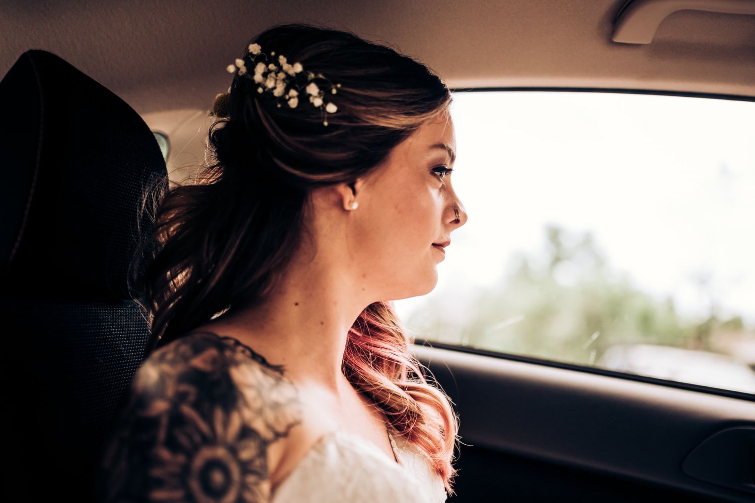 Side profile view of elegant bridal hairstyle with floral accessories in car.