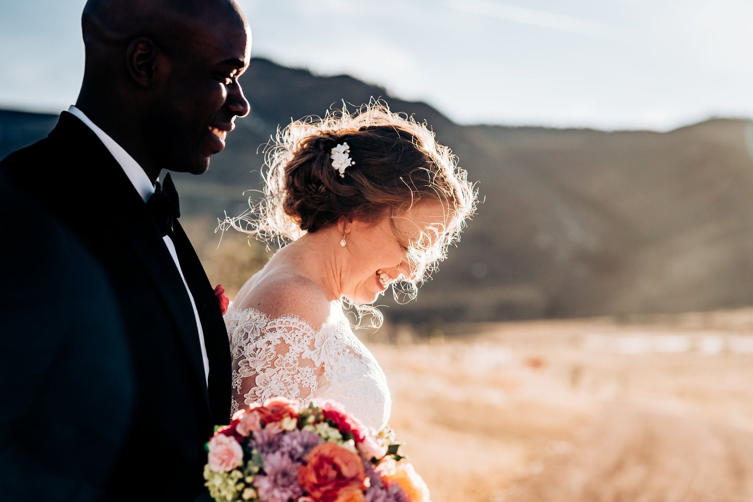 Candid moment of couple with colorful bouquet against mountain landscape.