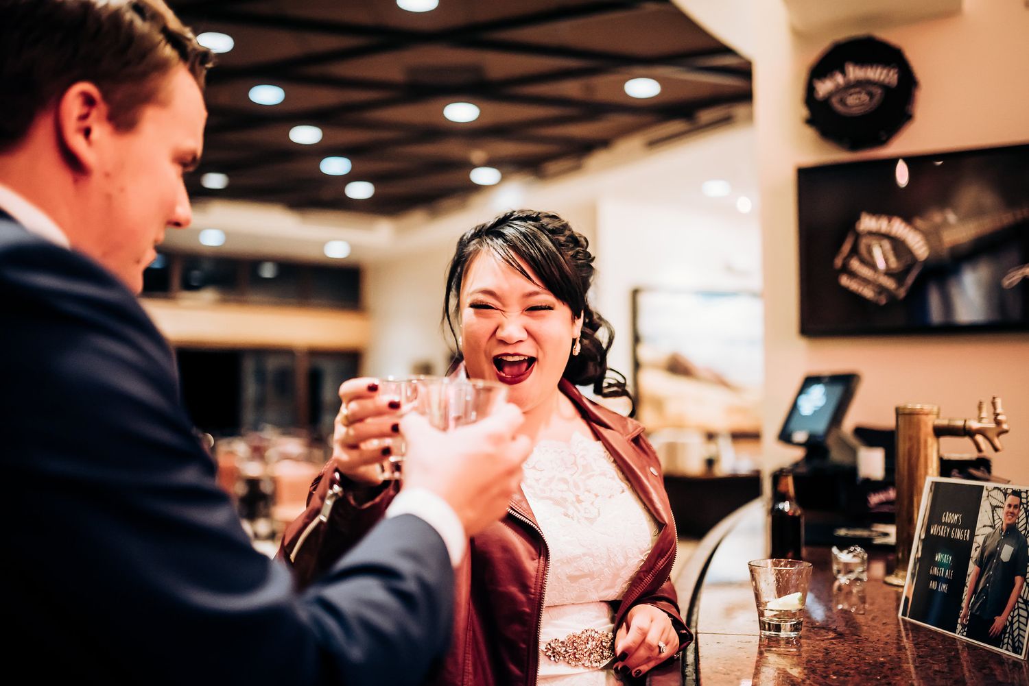 Couple sharing drinks and laughing together at a bar counter during a celebration.