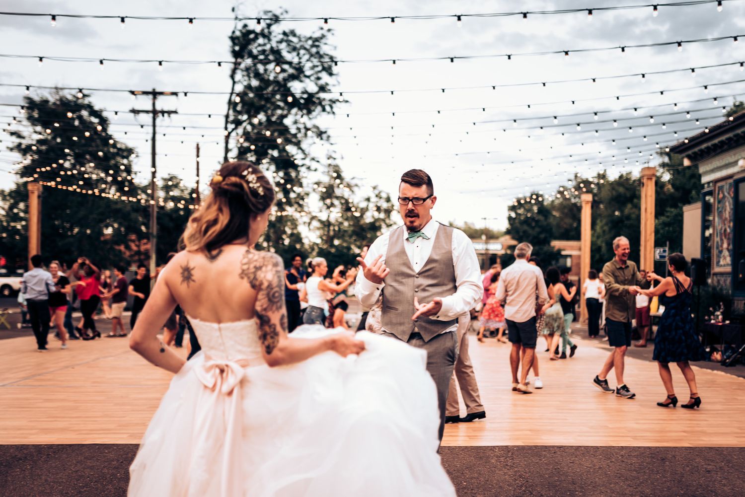 Dancing couple twirling on outdoor patio under festive string lights at reception.