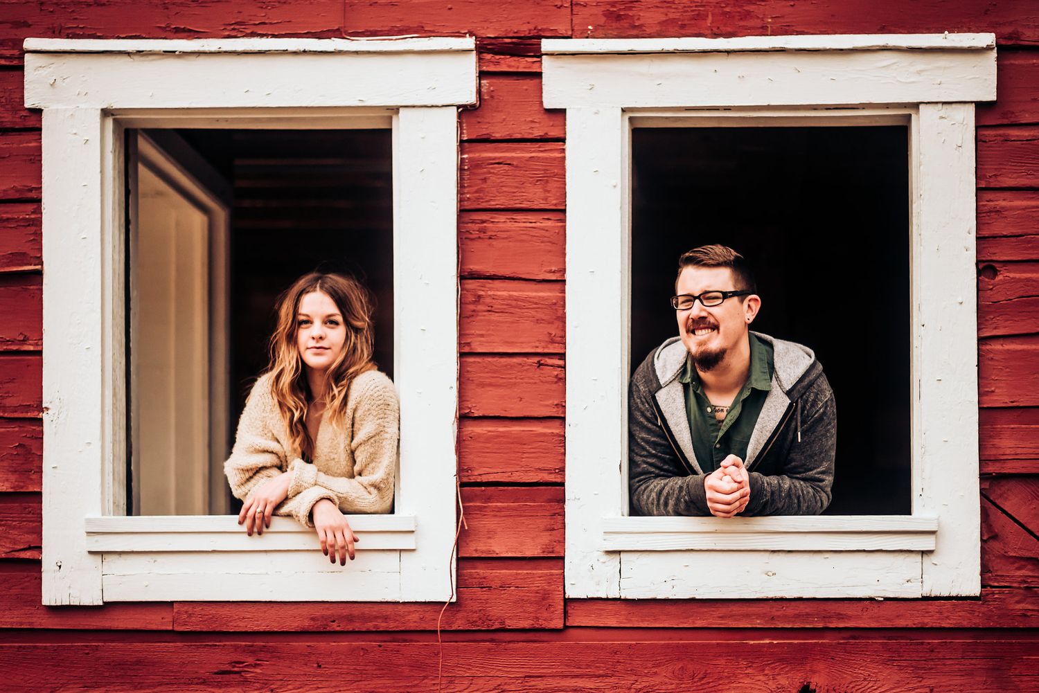 Two people lean out separate white-trimmed windows of a red building.