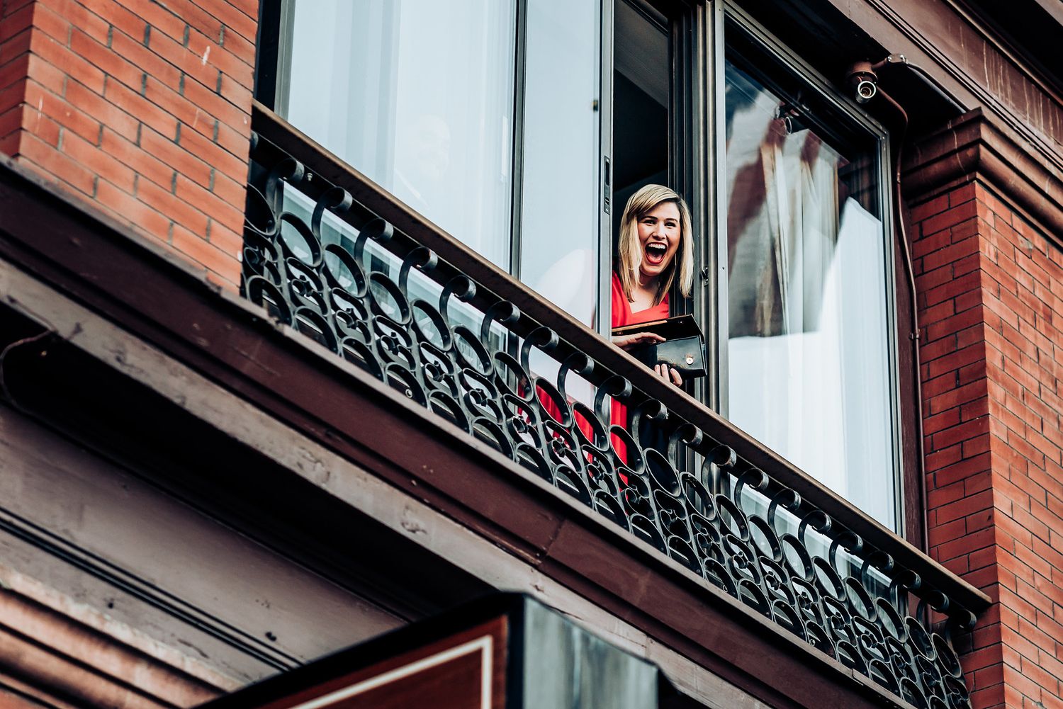 Wedding dress visible through ornate balcony window of brick building.
