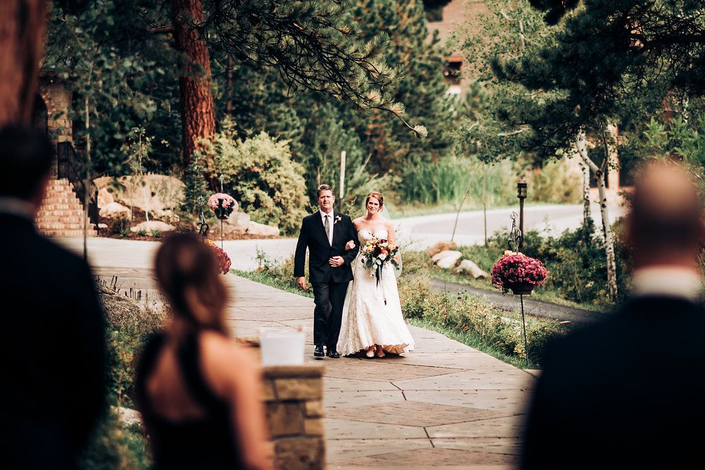 Wedding couple walking down stone pathway surrounded by pine trees.
