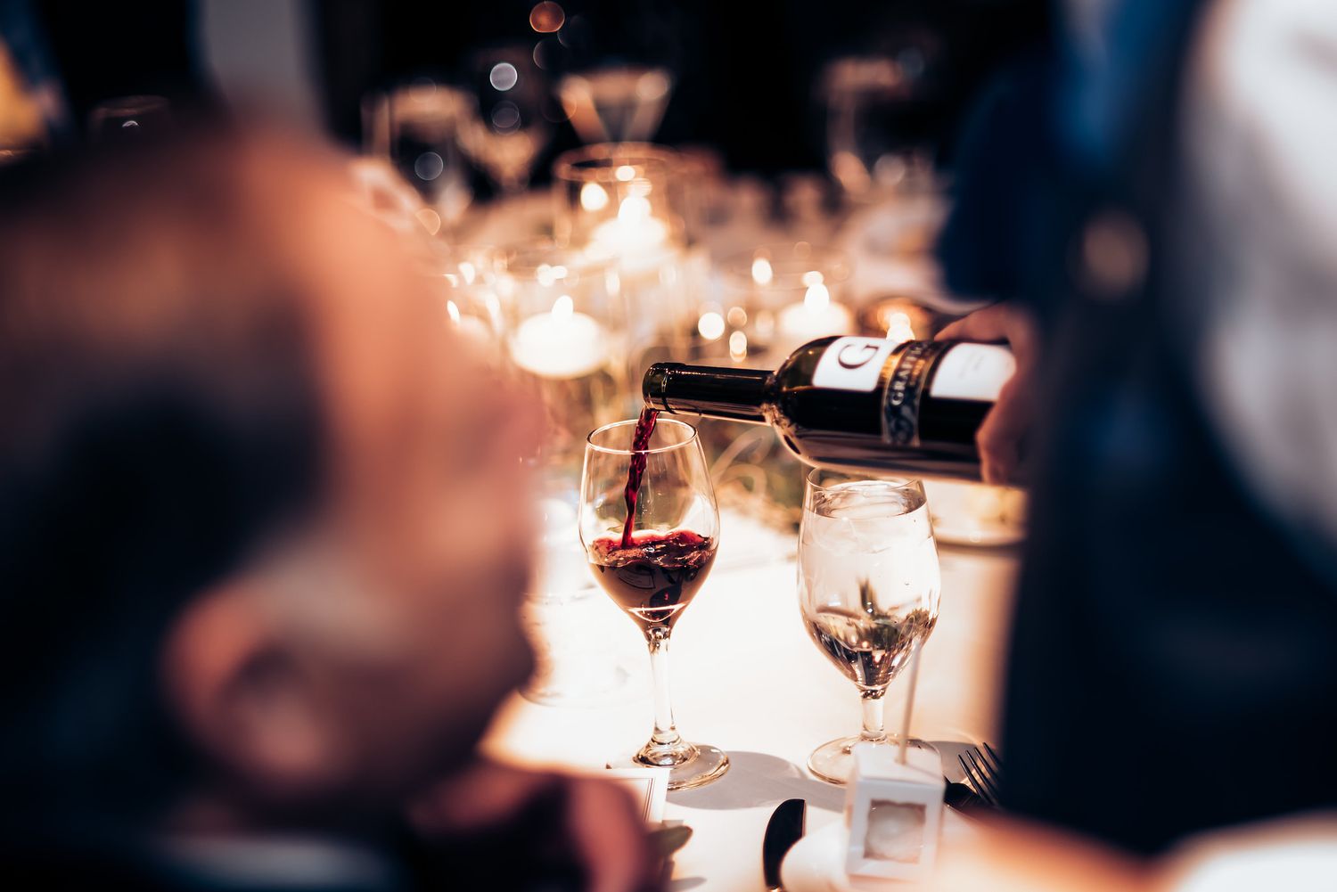 Red wine being poured into crystal glasses with ambient lighting creating a romantic atmosphere.