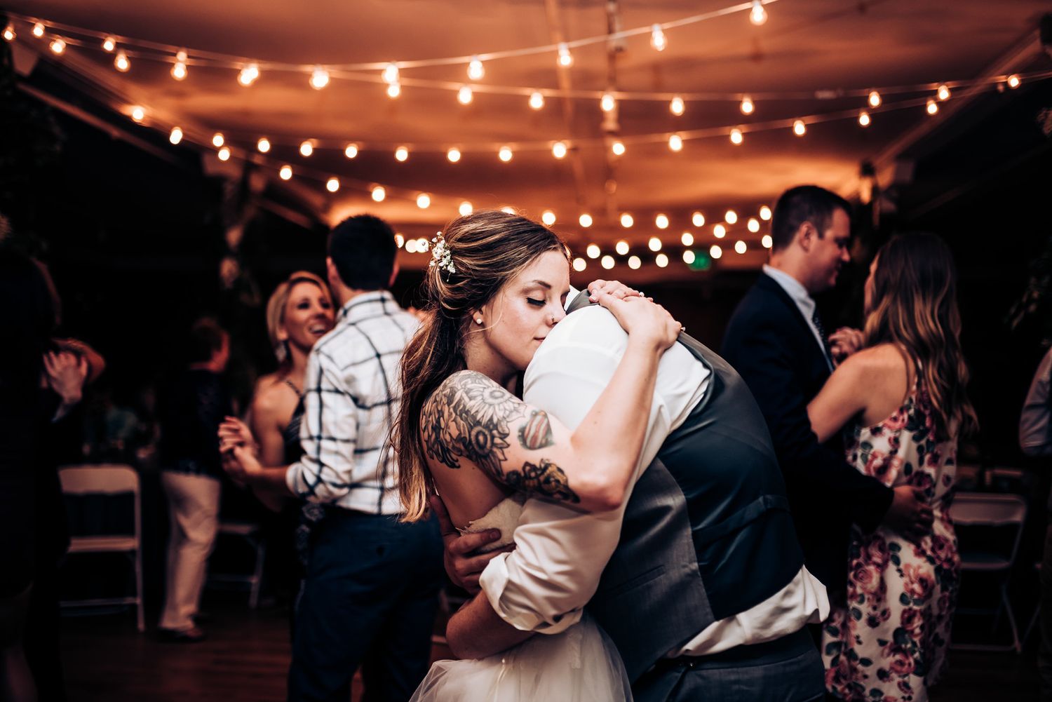 Intimate slow dancing moment captured under warm overhead string lights at a wedding reception.