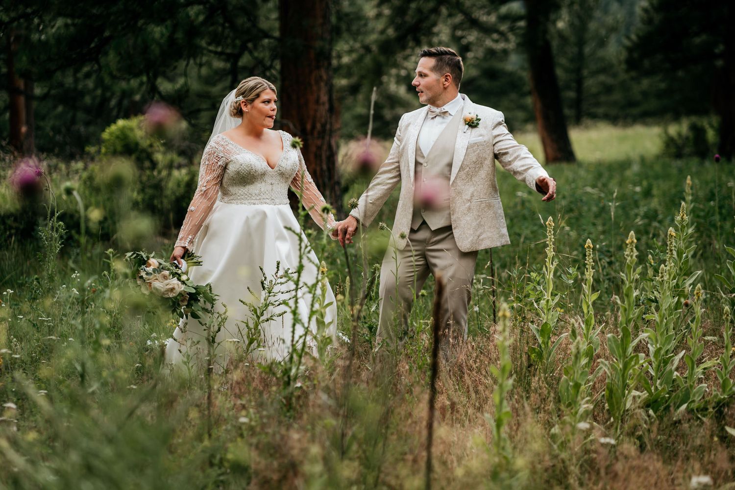 Wedding couple walking hand in hand through tall wildflowers in a meadow.