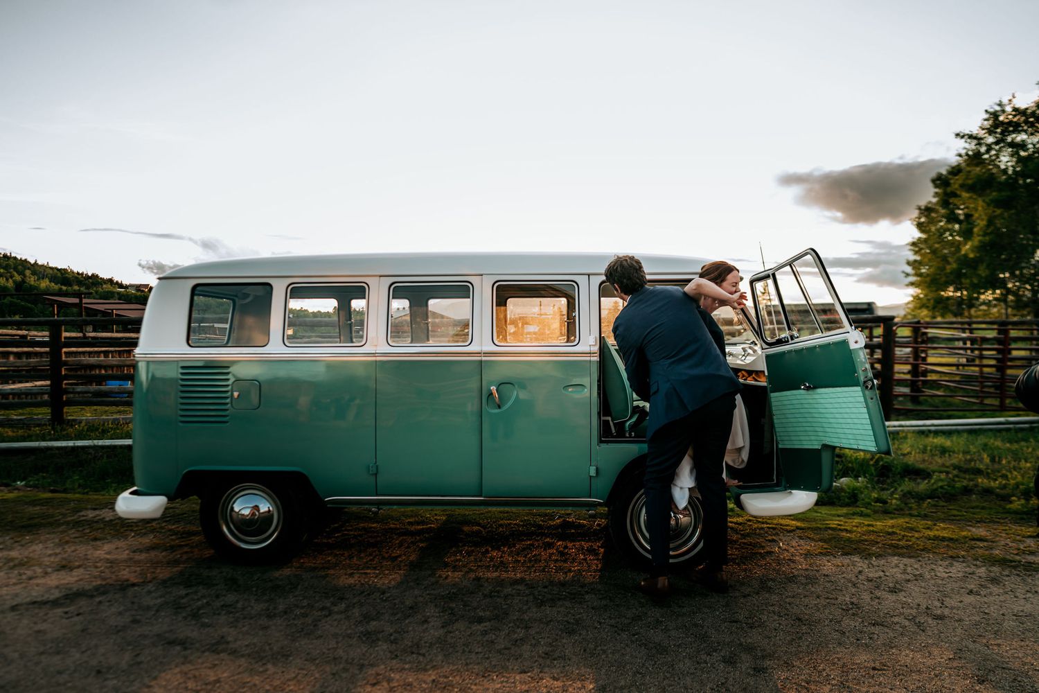 Person climbing into vintage turquoise Volkswagen van at sunset in rural setting.