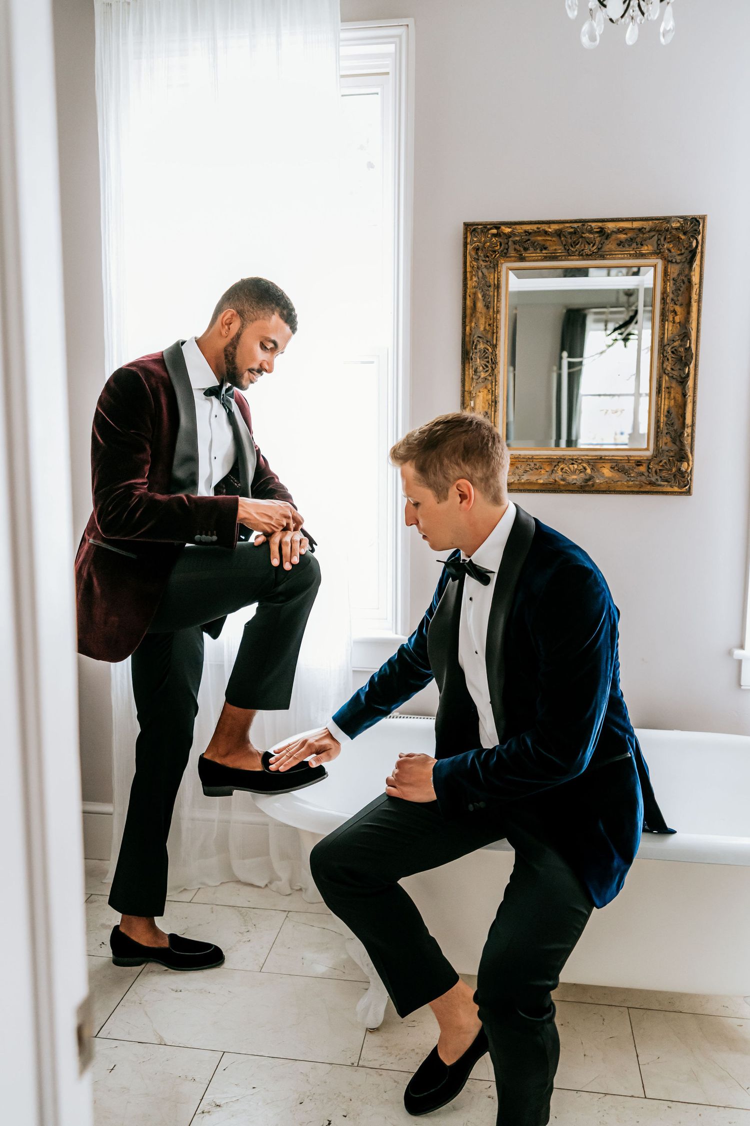 Two people in formal attire helping each other get ready in an elegant white room.