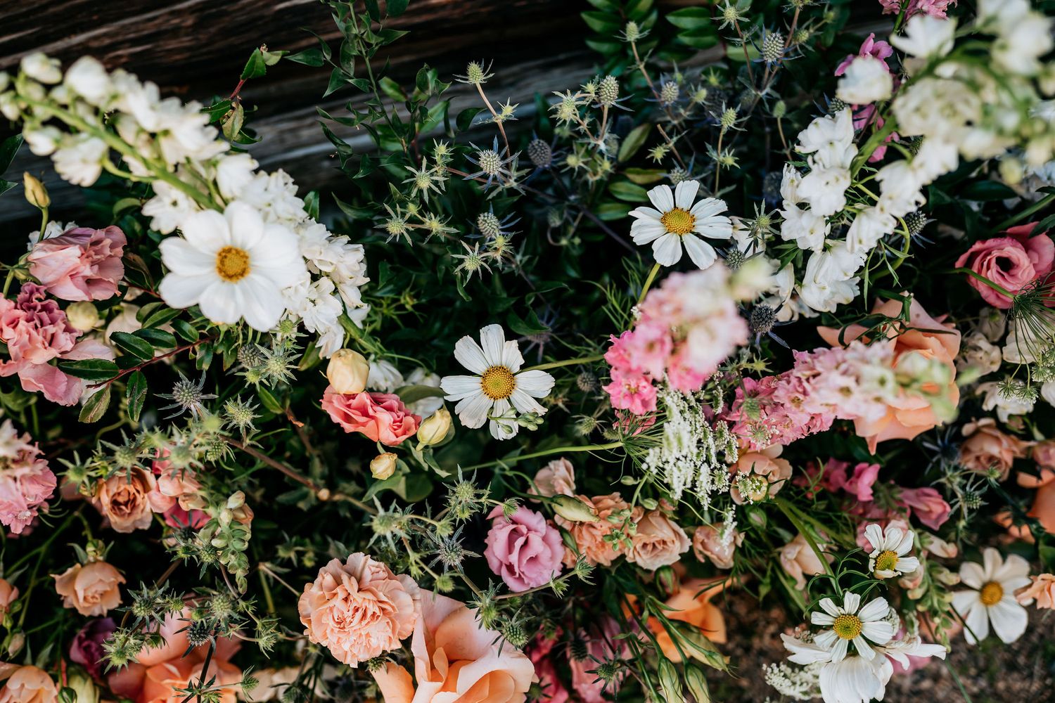 Colorful arrangement of pink roses, white daisies, and mixed flowers creating a romantic garden display.