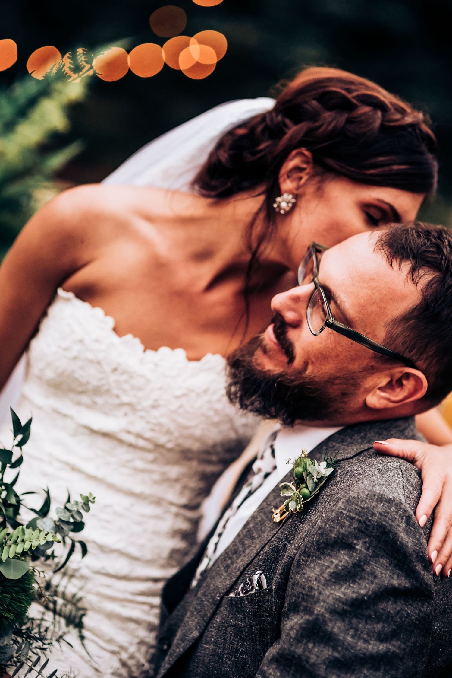 Intimate portrait of couple with bokeh lights and greenery in background.