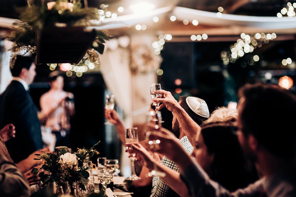 Wedding guests raise their glasses for a toast under sparkling string lights at reception.