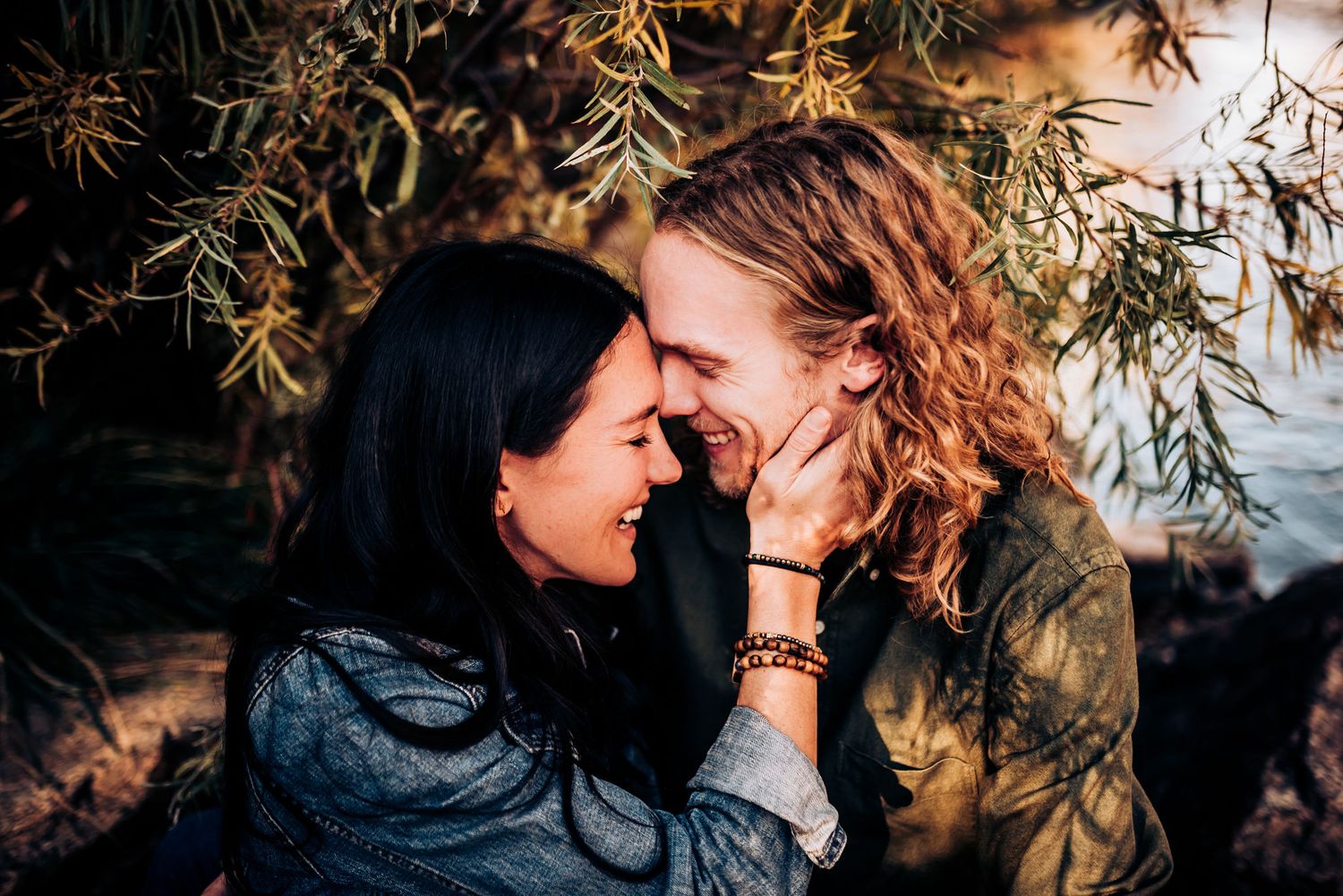 Romantic couple laughing together under tree branches at dusk.