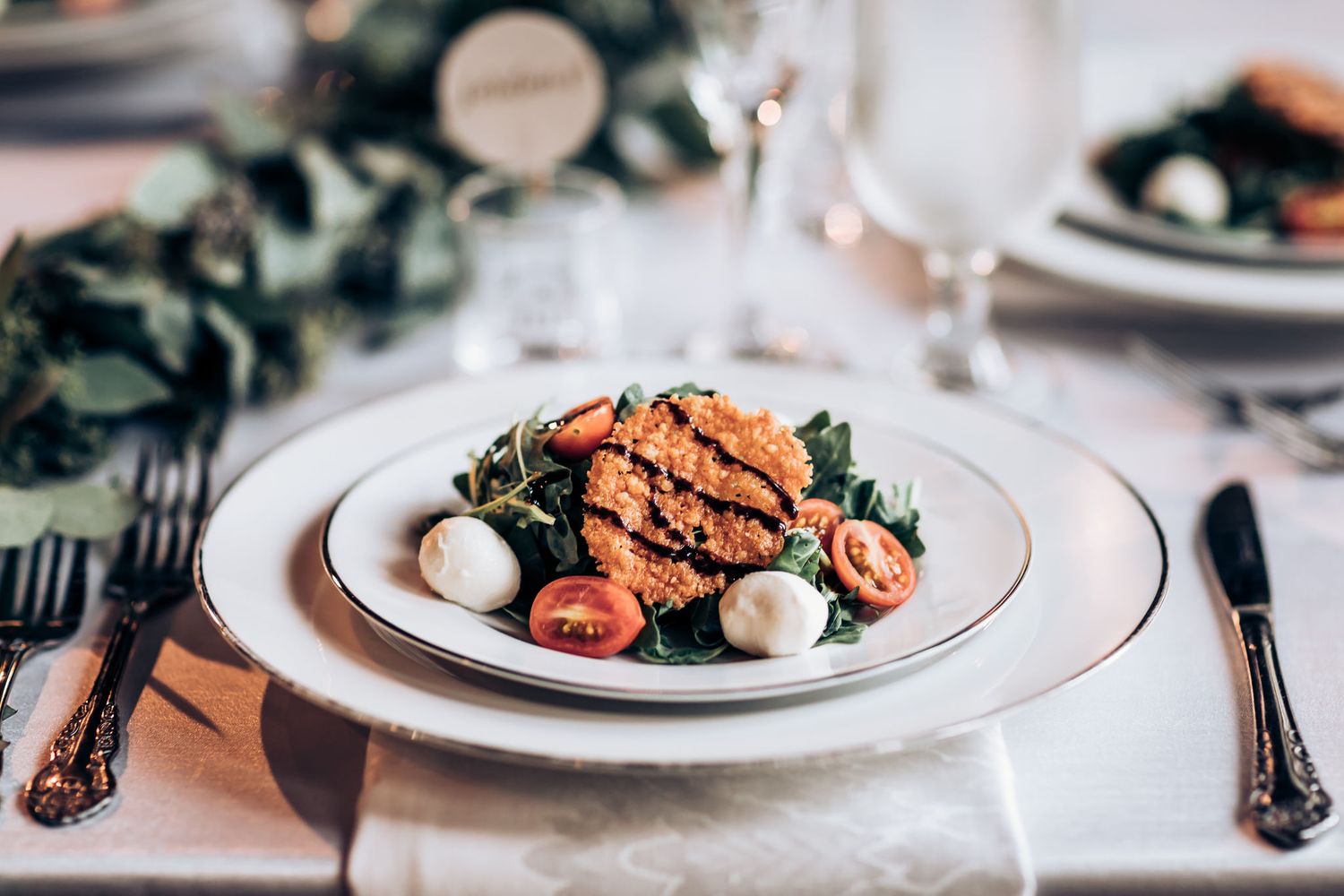 Gourmet salmon dish with greens and garnishes served on white china plates with formal place setting.