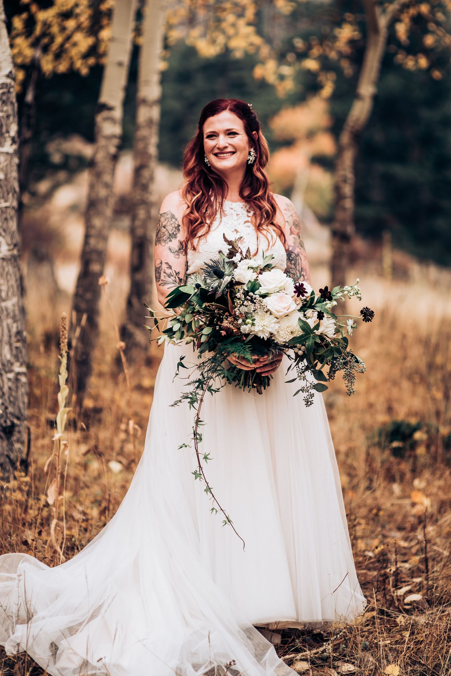 Wedding portrait in autumn forest with flowing white dress and cascading floral bouquet.