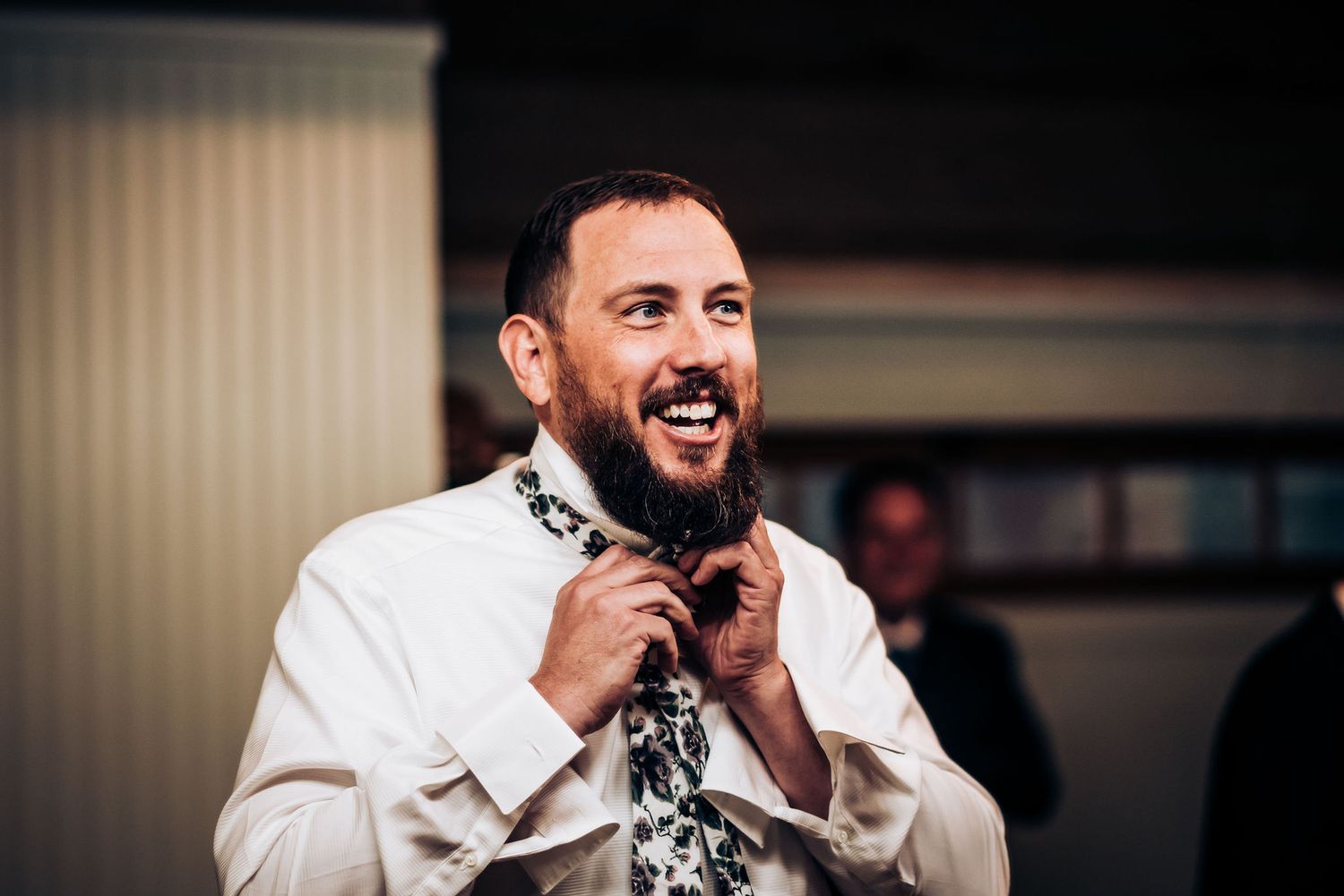 Person in white shirt and patterned tie adjusts collar with a smile.