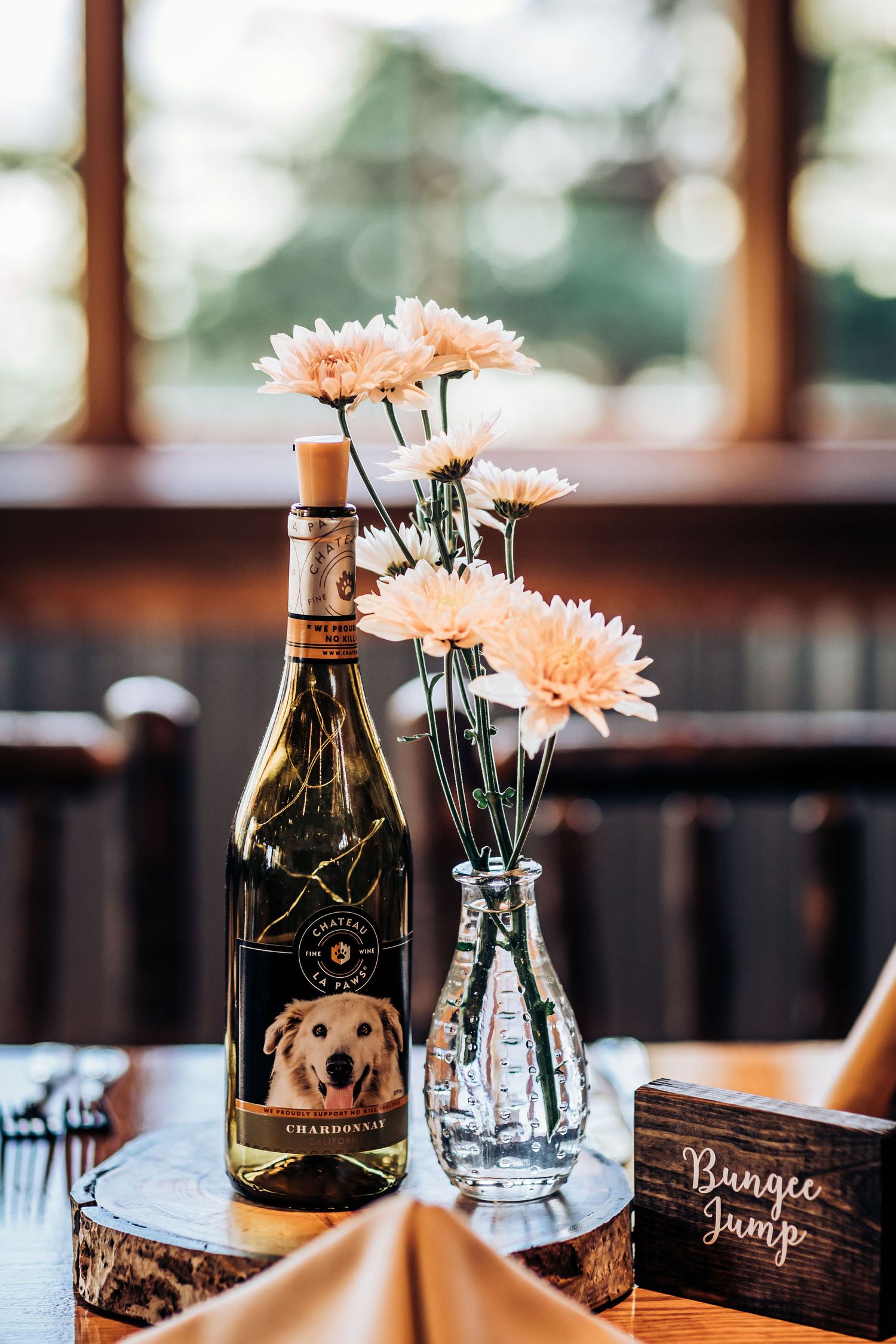 Custom wine bottle with dog label and pink daisies in crystal vase on reception table.