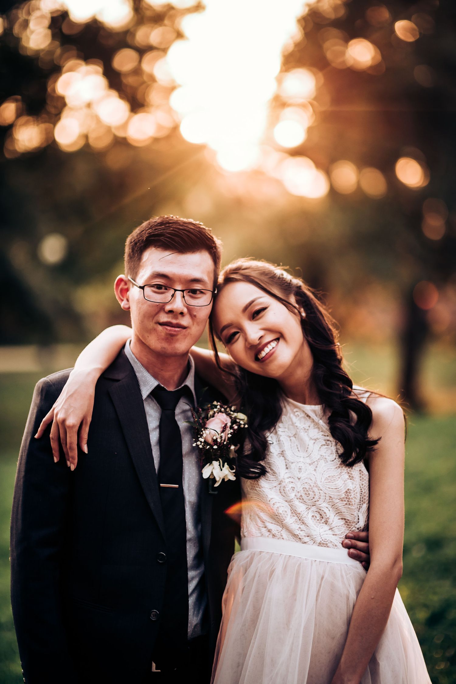A happy couple embraces while posing for a sunset portrait with glowing bokeh background.